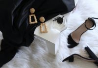 pair of gold-colored earrings on table and black ankle-strap pumps on area rug