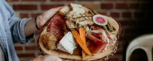 a person holding a platter of meats and cheeses